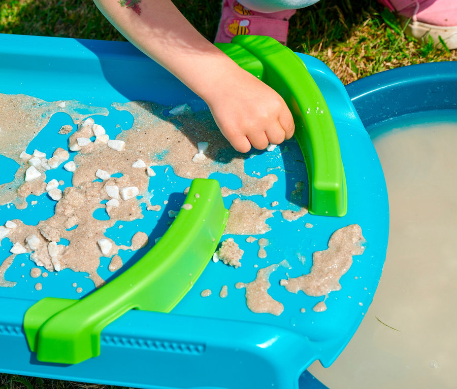 Kind spielt mit der blauen AquaPlay »Mudway STREAM« Matschbahn, die mit Sand, Wasser und weißen Steinen gefüllt ist.