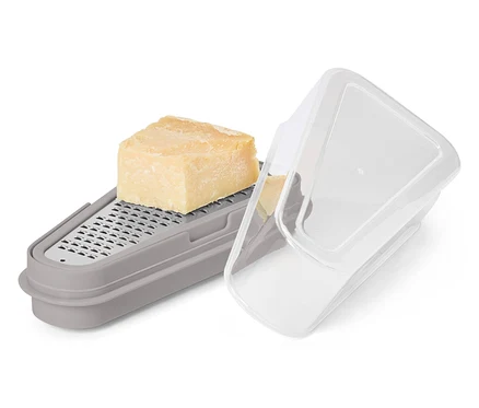 Ein Stück Käse liegt auf einer grauen Reibe mit Behälter und transparentem Deckel.