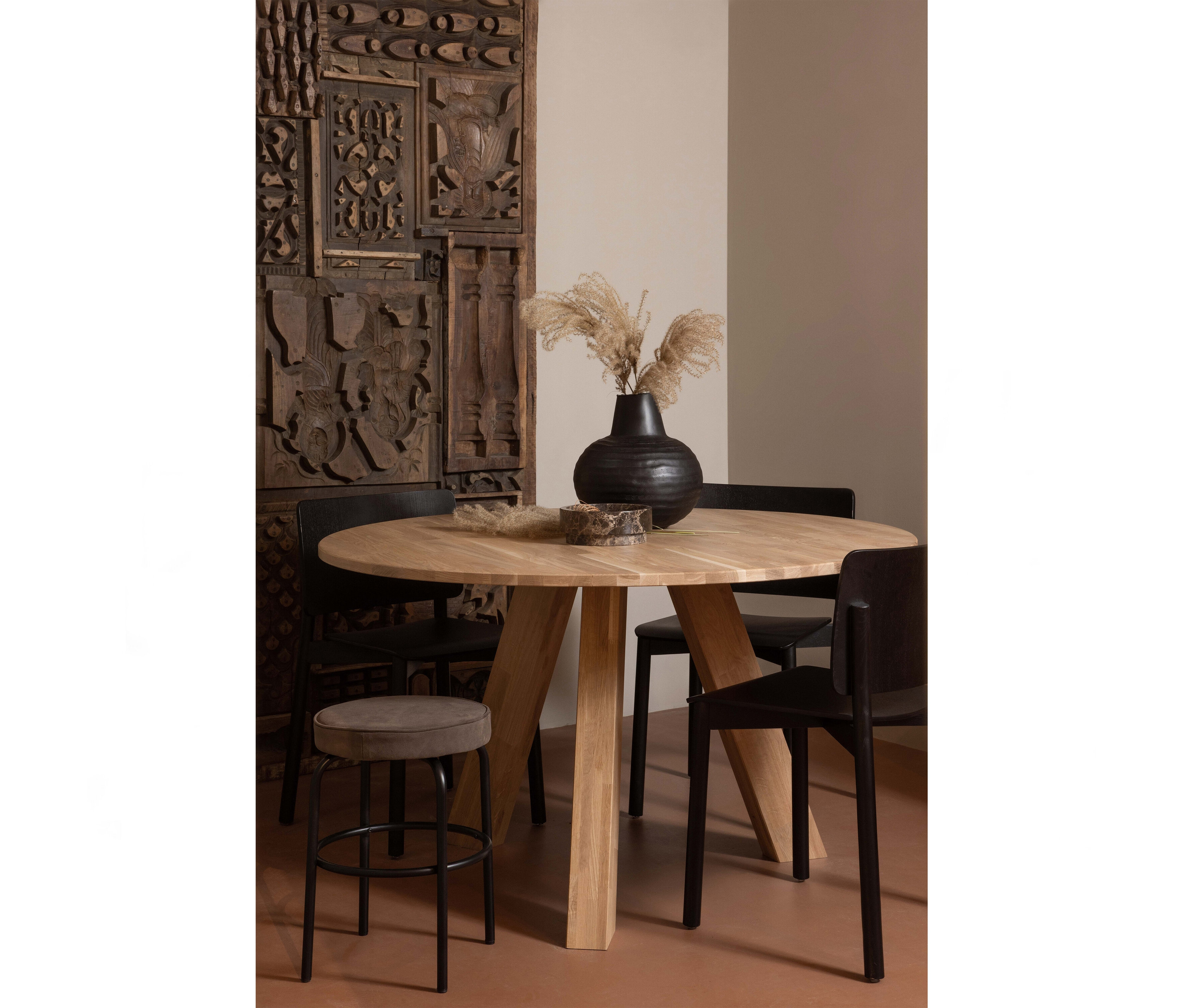 Runder, heller WOOOD »Rhonda« Esstisch, ca. 129 cm, mit schwarzer Vase und Deko auf braunem Boden, umgeben von Stühlen und einem Hocker.