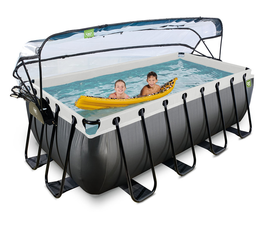 Zwei Kinder in einem rechteckigen EXIT Pool-Set, Lederoptik, 400 x 200 cm, mit transparenter Abdeckung. Ein Mädchen lächelt, während es sich an einem gelben Schlauchboot festhält, neben einem Jungen.