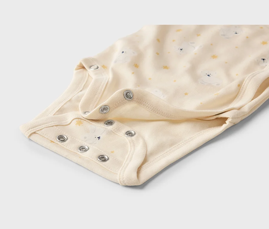 Cremefarbener Baby-Body mit einem Muster aus weißen Teddybären und gelben Sternen. Silberne Druckknöpfe sind im Schrittbereich sichtbar.