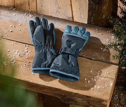Dunkelblaue Winterhandschuhe mit hellblauen Akzenten, elastischen Bündchen und verstellbaren Riemen, auf einer Holzoberfläche mit Schneeflocken und grünem Laub.