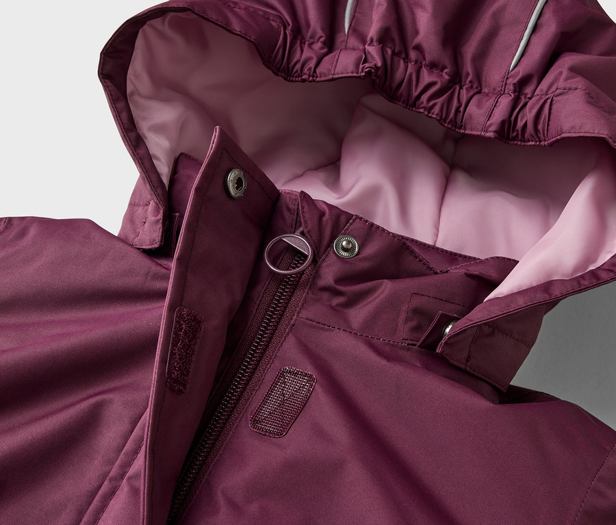 Dunkelrote Jacke mit Kapuze, Reißverschluss und Druckknöpfen. Die Kapuze hat ein hellrosa Futter und einen reflektierenden Streifen.