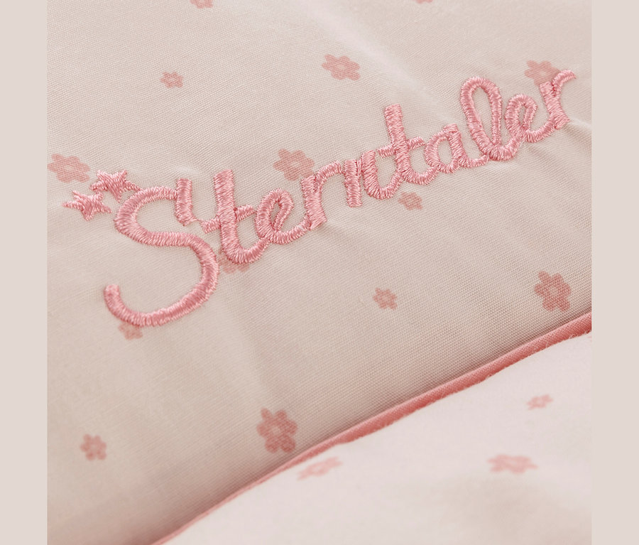 Nahaufnahme eines hellrosa Stoffes mit zartem Blumenmuster und dem gestickten Schriftzug „Sterntaler“ in dunklerem Rosa.