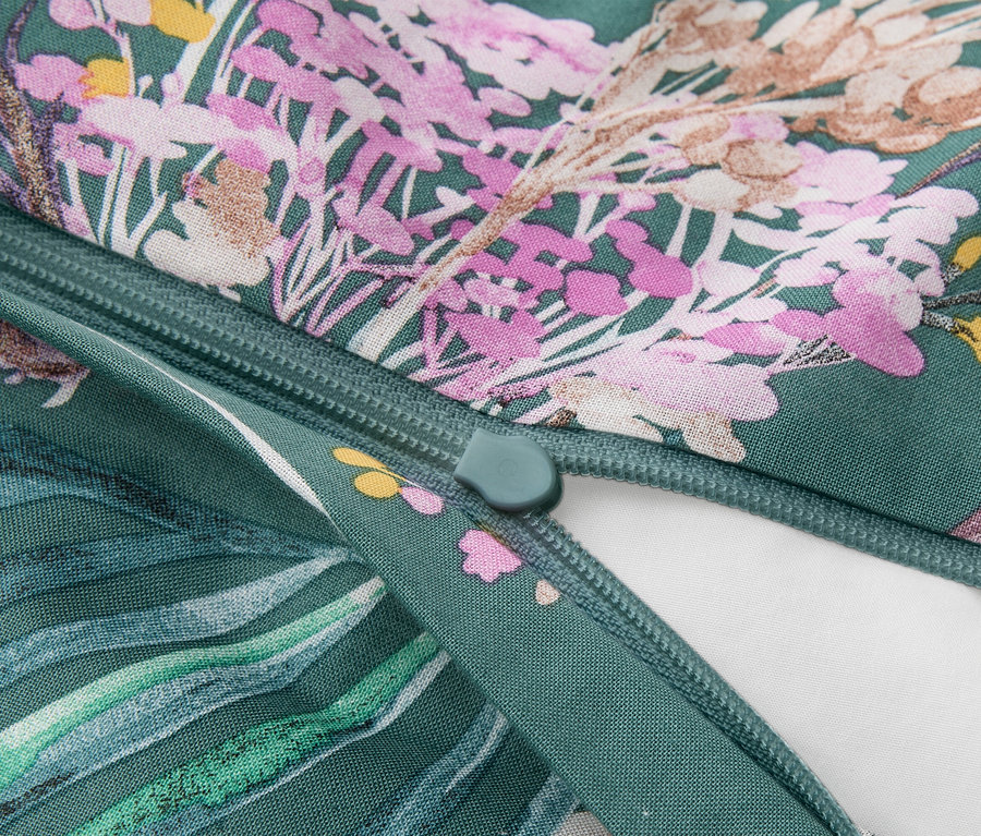 Nahaufnahme eines grünen Stoffes mit Blumenmuster in Rosa, Lila, Gelb und Braun, mit einem teilweise geöffneten grünen Reißverschluss, der ein weißes Futter zeigt.