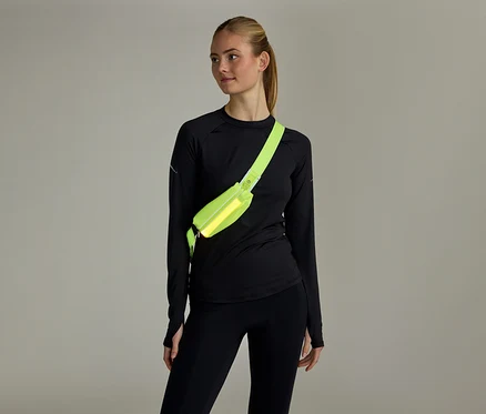 Frau mit Pferdeschwanz, schwarzem Langarmshirt und Leggings, trägt eine neongelbe Bauchtasche quer über der Brust.