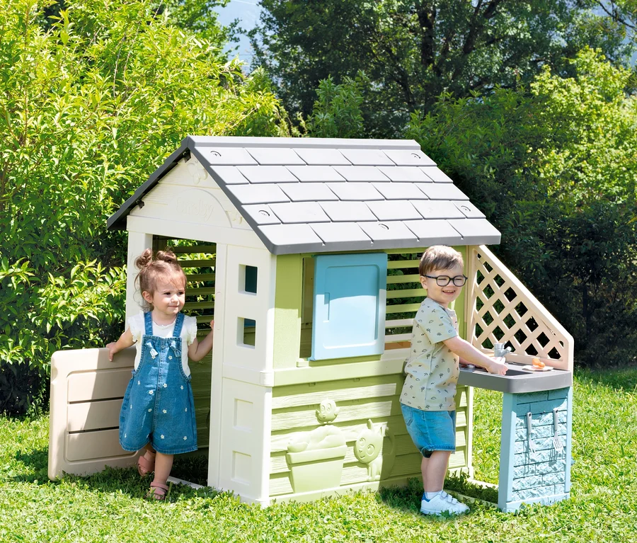 Zwei Kinder spielen im Garten vor dem Smoby Life Spielhaus »Pretty« mit Küche.