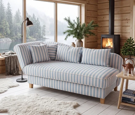 Blau-weiß gestreifte Récamiere mit Kissen in holzgetäfeltem Raum. Große Fensterfront mit Blick auf See und Wald. Brennender Kaminofen, Stehlampe und flauschige Teppiche.
