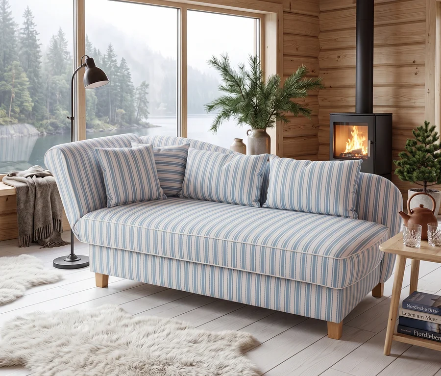 Blau-weiß gestreifte Récamiere mit Kissen in holzgetäfeltem Raum. Große Fensterfront mit Blick auf See und Wald. Brennender Kaminofen, Stehlampe und flauschige Teppiche.