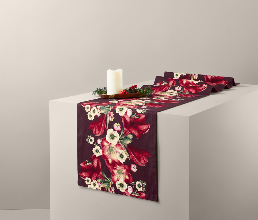Auf einem weißen Sockel liegt ein bordeauxroter Tischläufer mit Blumenmuster und einer Kerze.