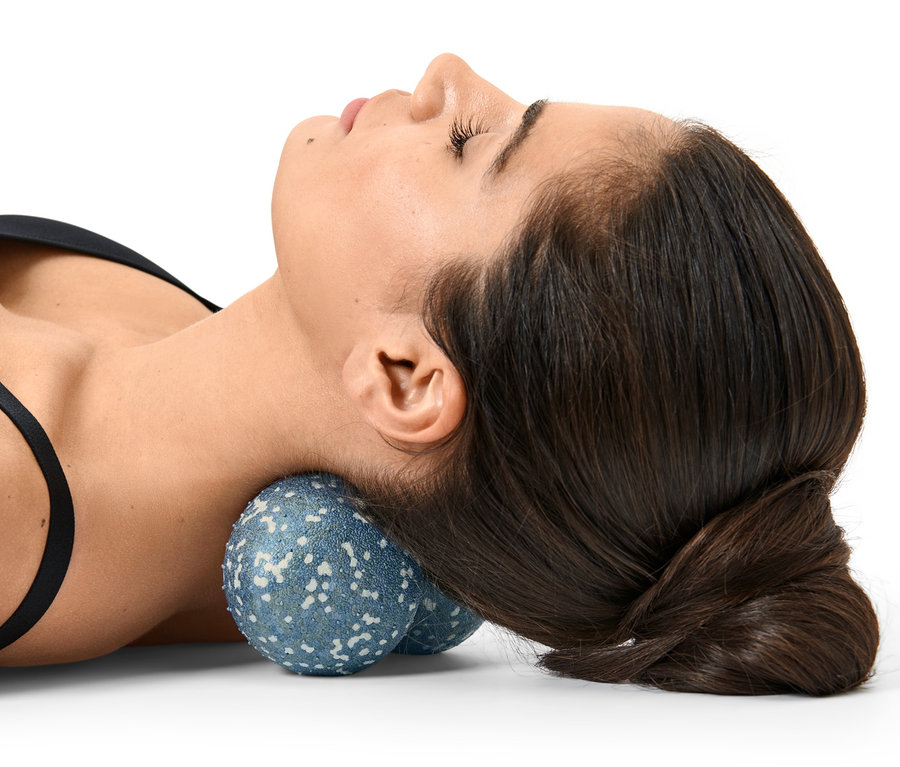 Eine Frau liegt auf dem Rücken und hat einen Duo-Massageball unter ihrem Nacken.