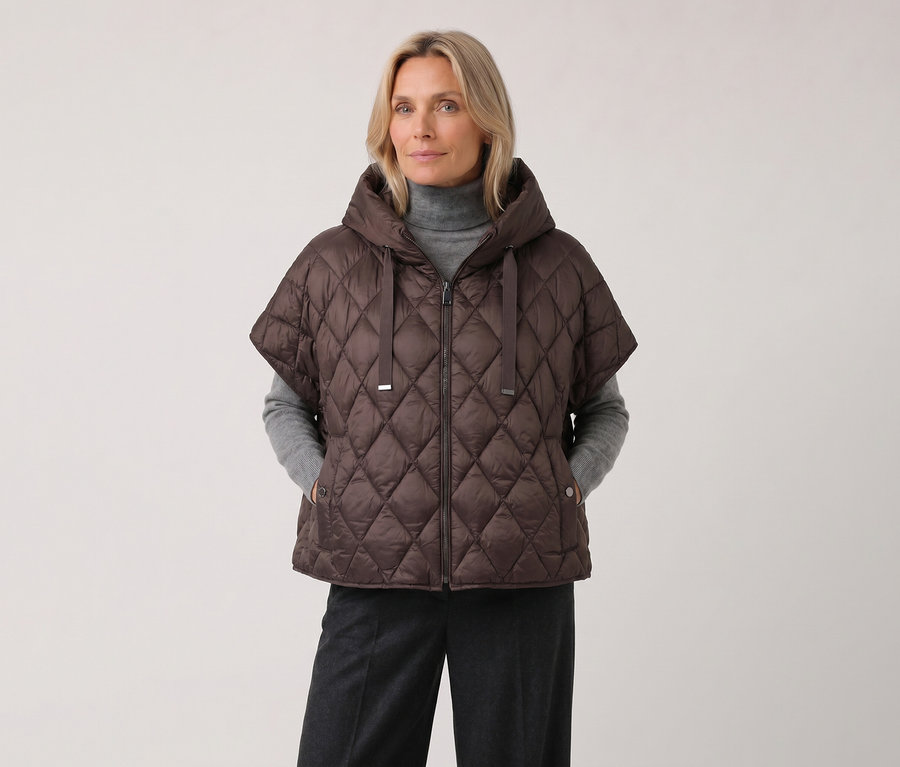 Eine blonde Frau trägt eine braune Barbara Lebek Steppweste mit Kapuze und kurzen Ärmeln über einem grauen Rollkragenpullover und einer dunklen Hose.