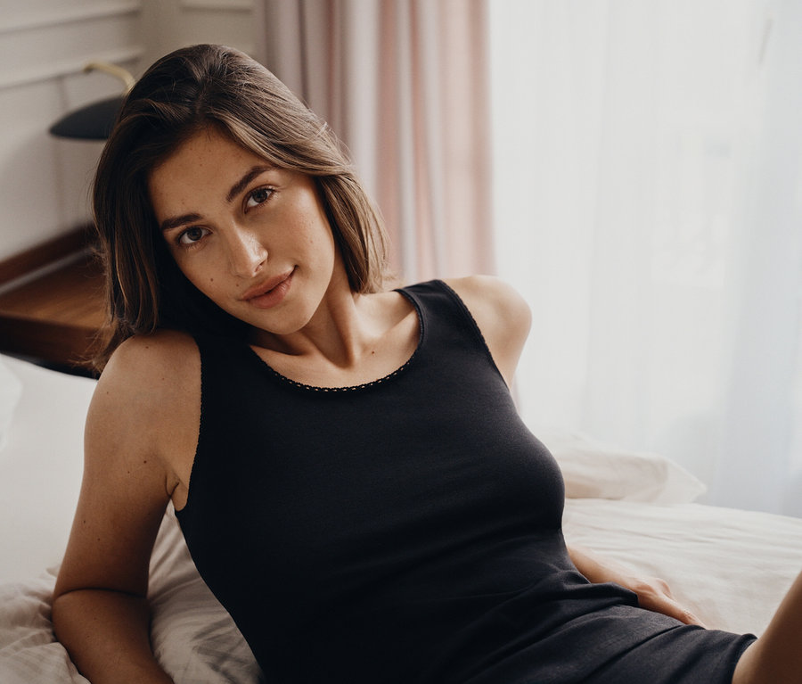Porträt einer Frau, die in einem schwarzen Tanktop auf einem Bett liegt.