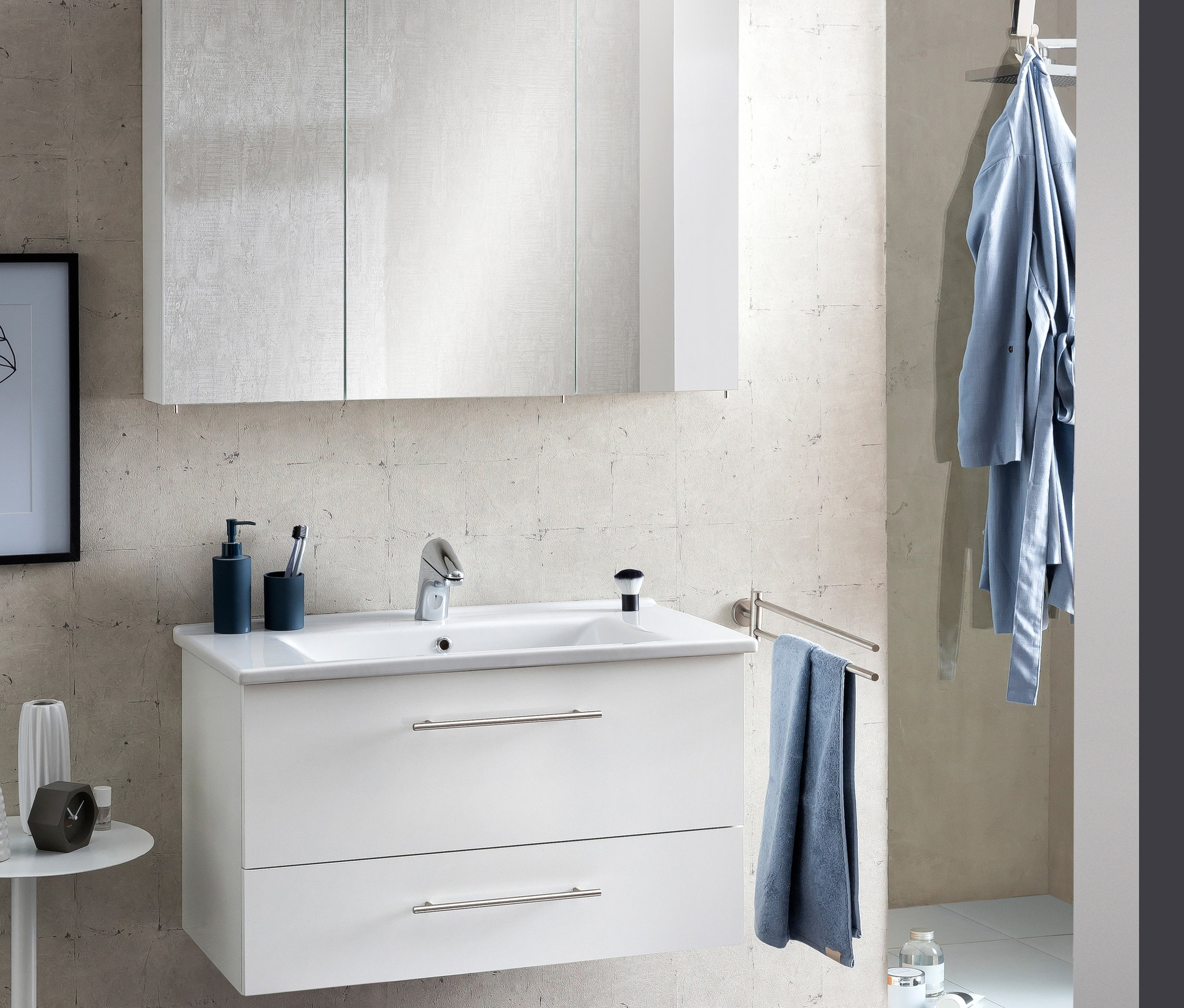 Weißes Badezimmer mit Waschbecken mit zwei Schubladen, einem Spiegelschrank »Runa SPS Irene 1000.1« in Weißglänzend und einem blauen Handtuch.