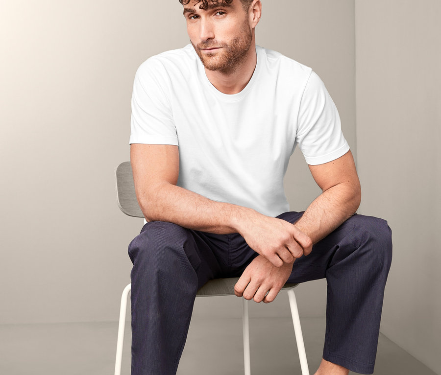 Mann sitzt auf einem Stuhl und trägt ein weißes T-Shirt und blaue Hosen. Er trägt eines von zwei T-Shirts mit Rundhalsausschnitt.