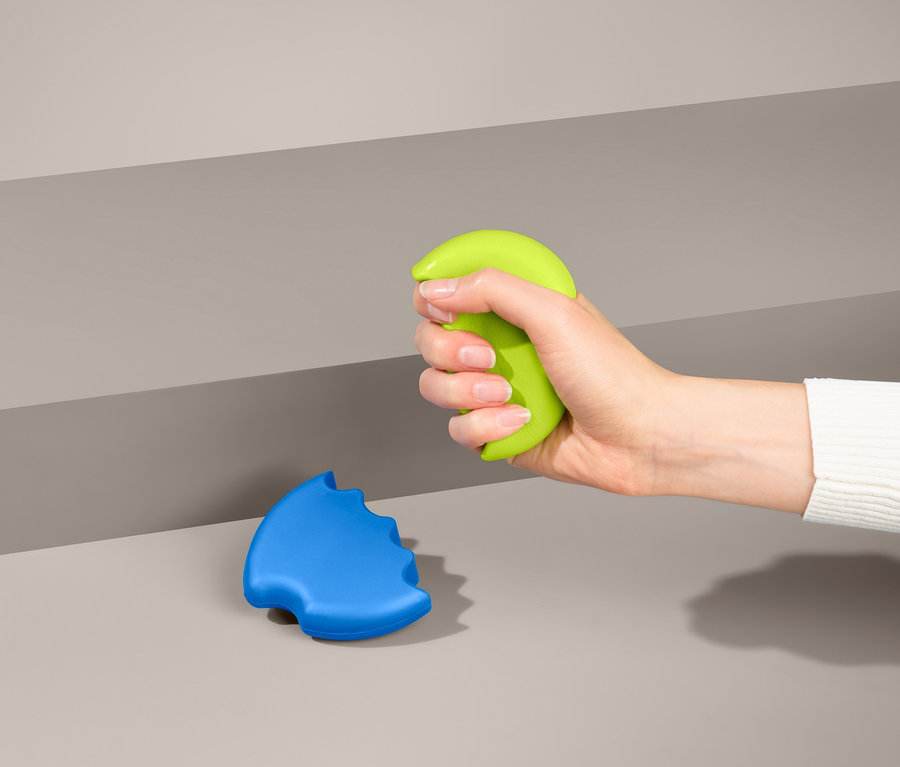 Eine Hand drückt einen grünen Handtrainer, daneben liegt ein blauer Handtrainer.