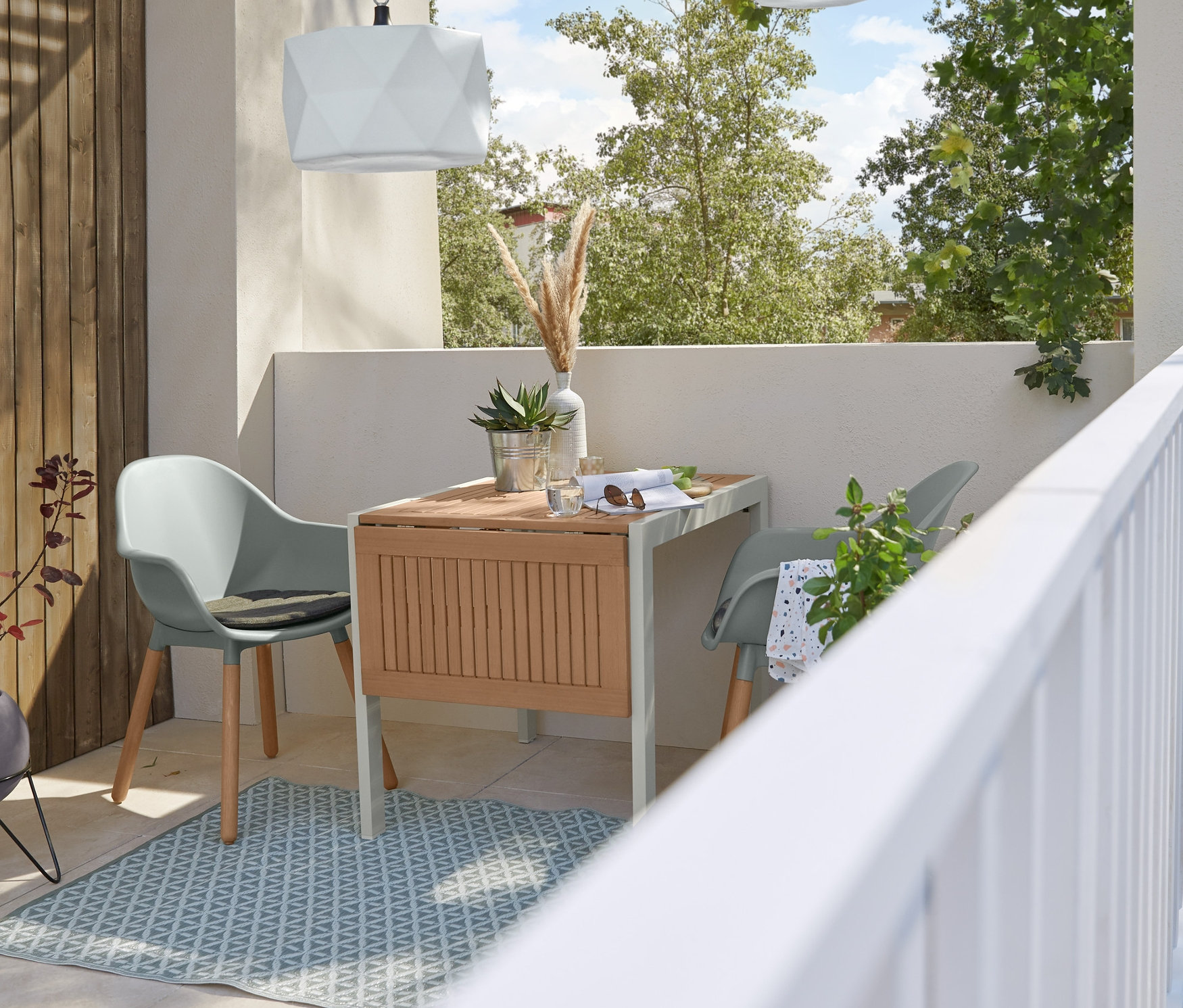 Zwei graue Garten-Schalenstühle stehen an einem Ausziehtisch auf einem Outdoorteppich unter einer LED-Hängeleuchte.