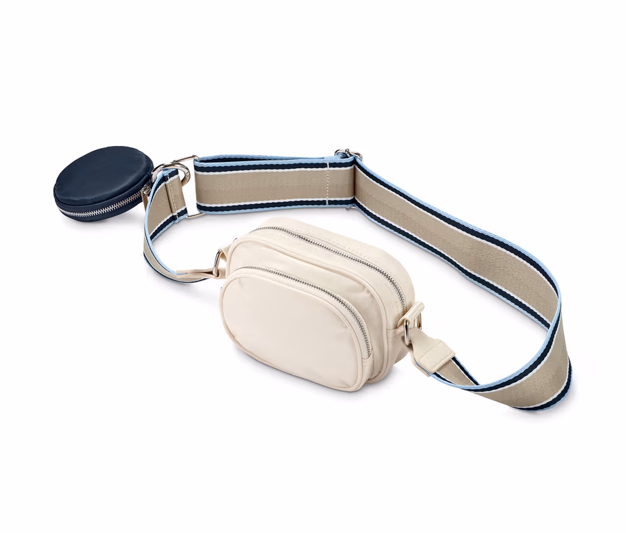 Eine cremefarbene Crossbody-Tasche mit einem marineblauen Reissverschlussetui und einem Riemen mit beigen, weißen und blauen Streifen.