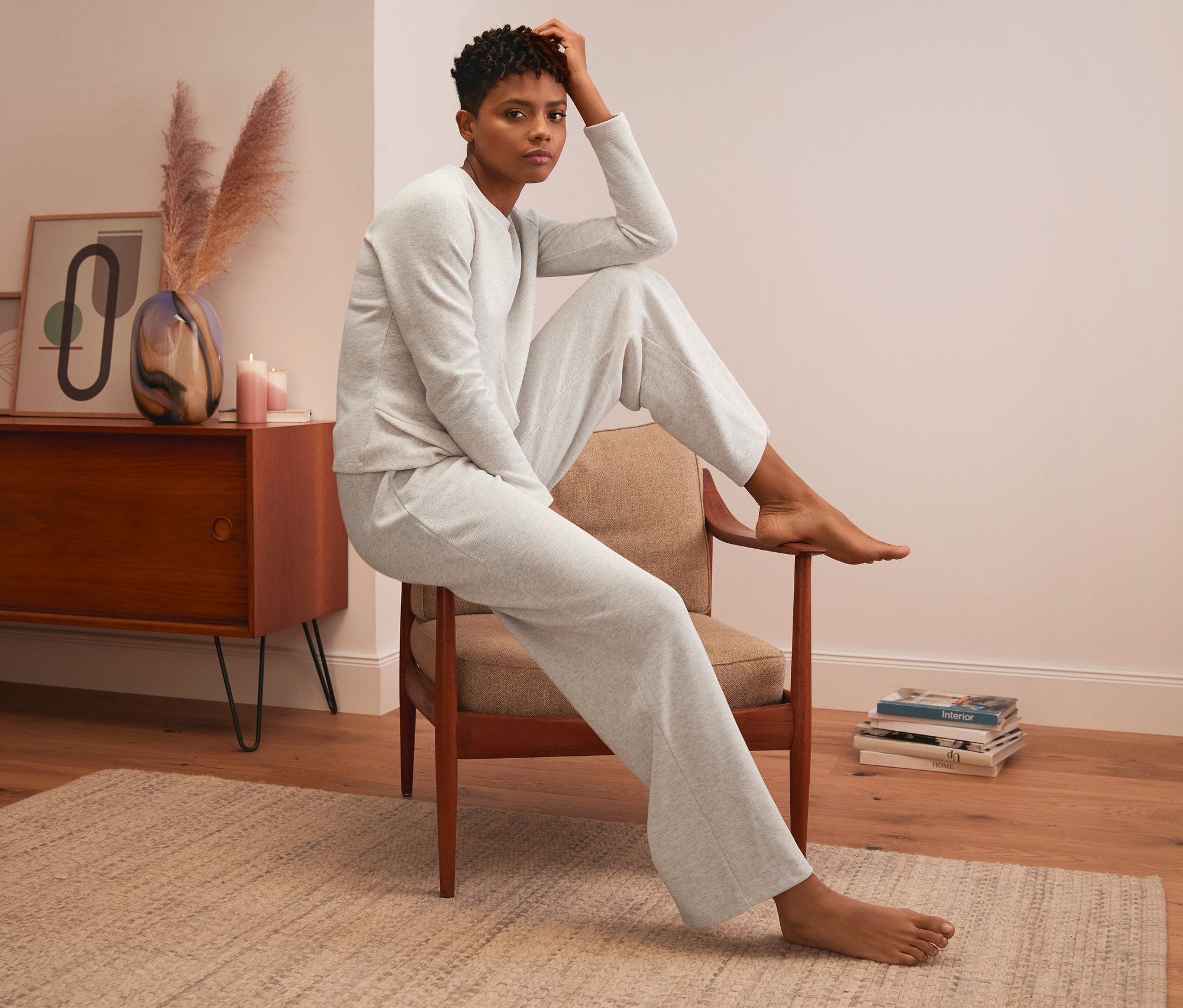 Frau sitzt auf einem Stuhl und trägt eine Loungewear-Hose und ein Oberteil.