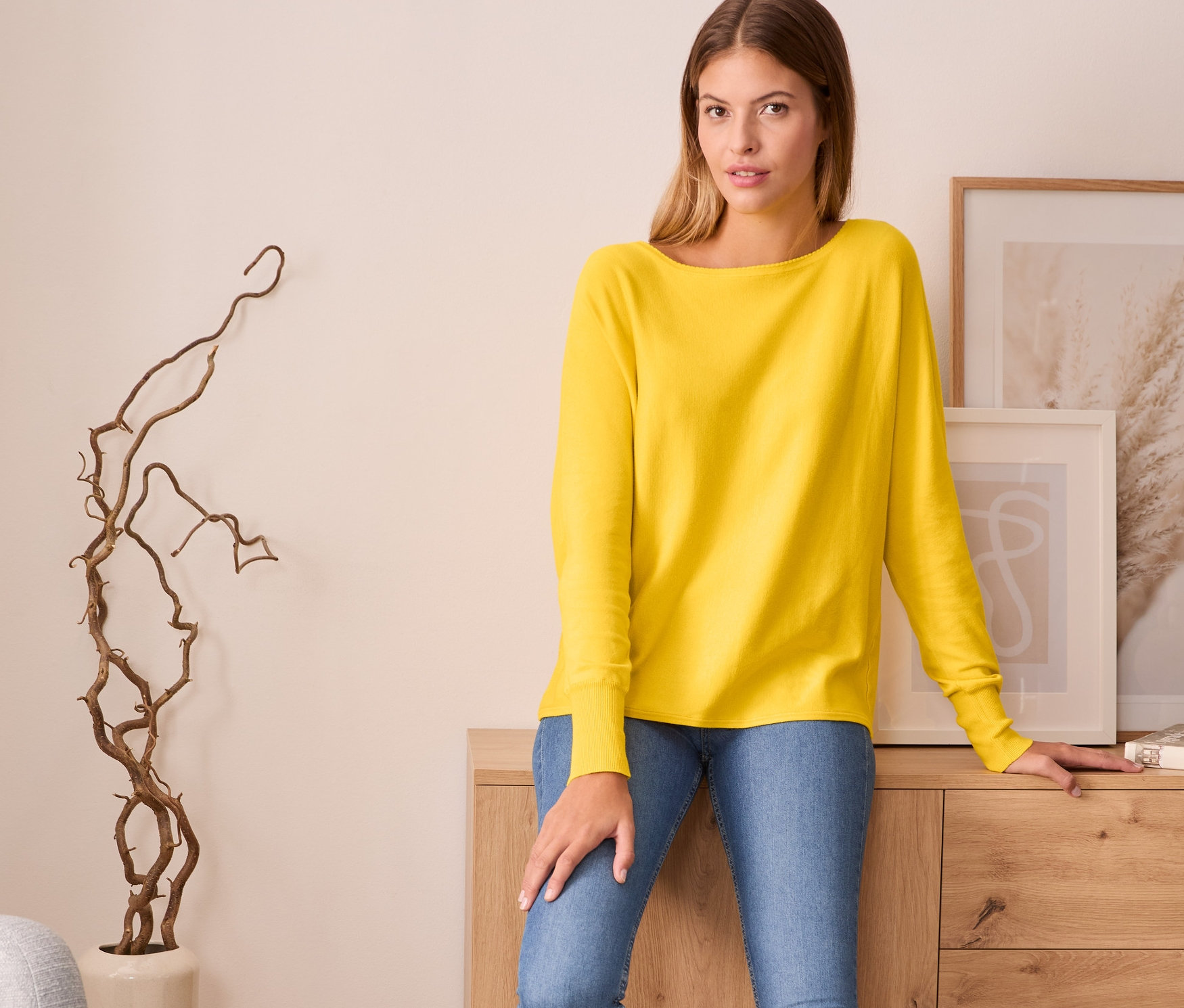 Frau posiert in Feinstrickpullover in Gelb, blauen Jeans und weißen Turnschuhen.