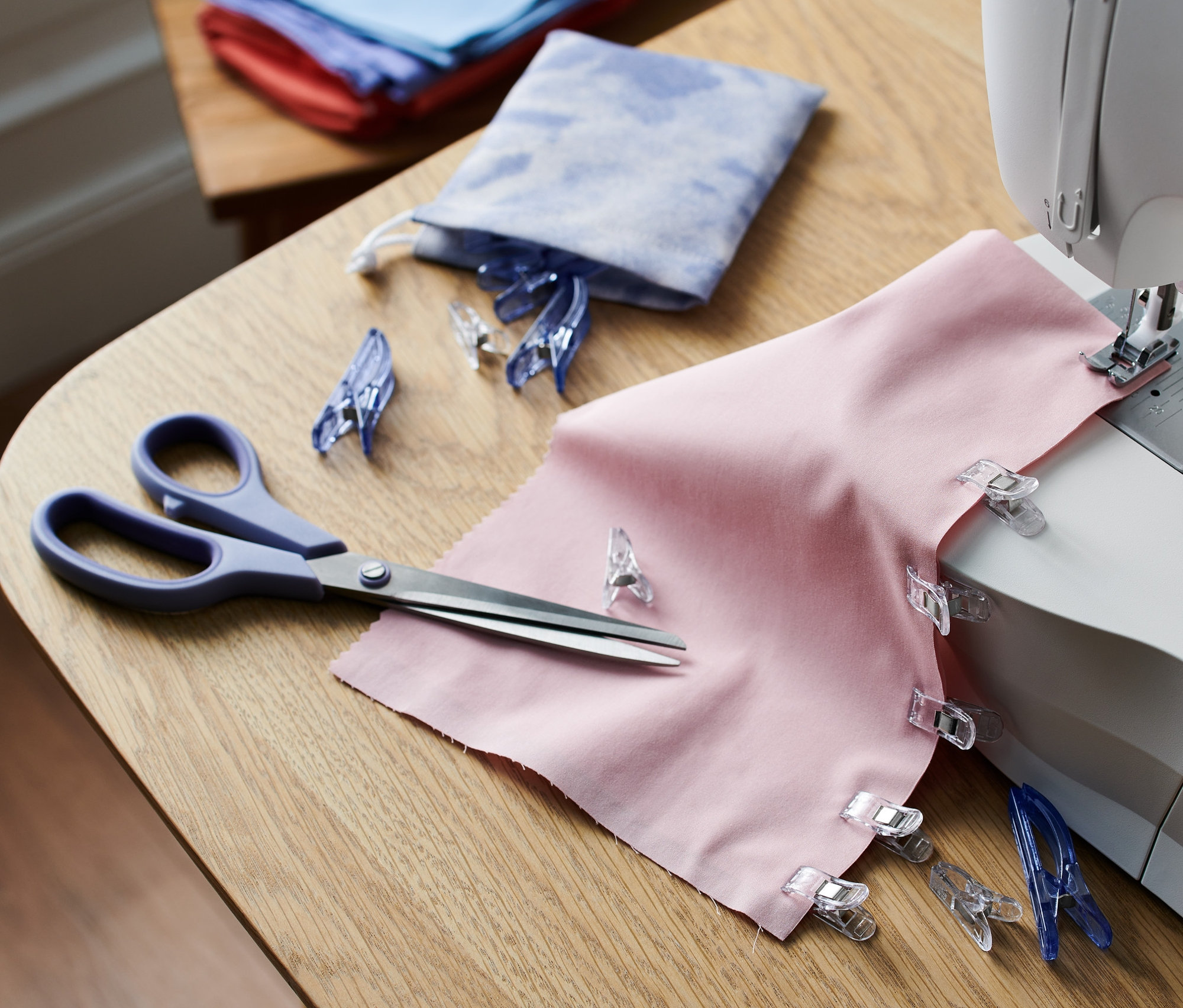 Rosafarbener Stoff mit 20 Stoffklammern an einer Nähmaschine.