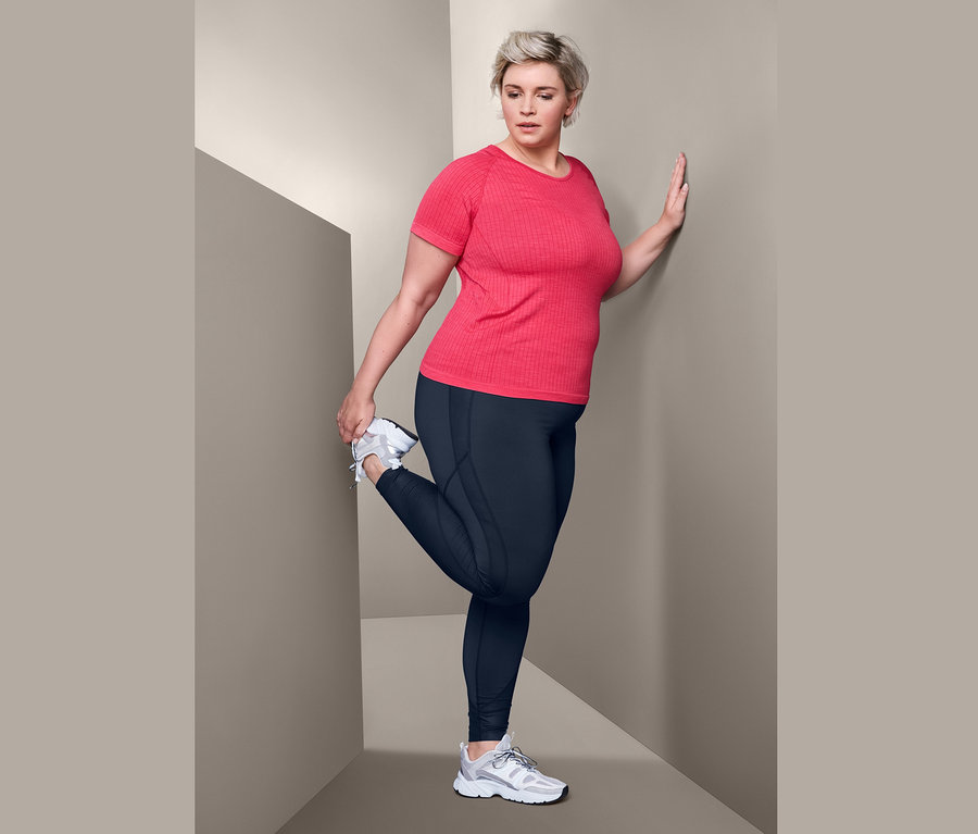 Frau dehnt Bein in rotmeliertem Seamless-Funktionsshirt und Bodyforming-Sporttights.