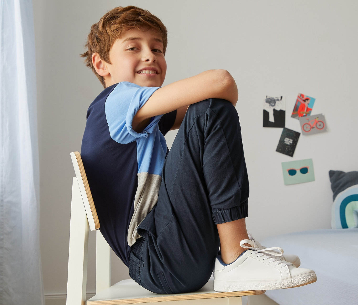 Junge sitzt auf einem Stuhl und trägt eine dunkelblaue Chino im Jogger-Style.