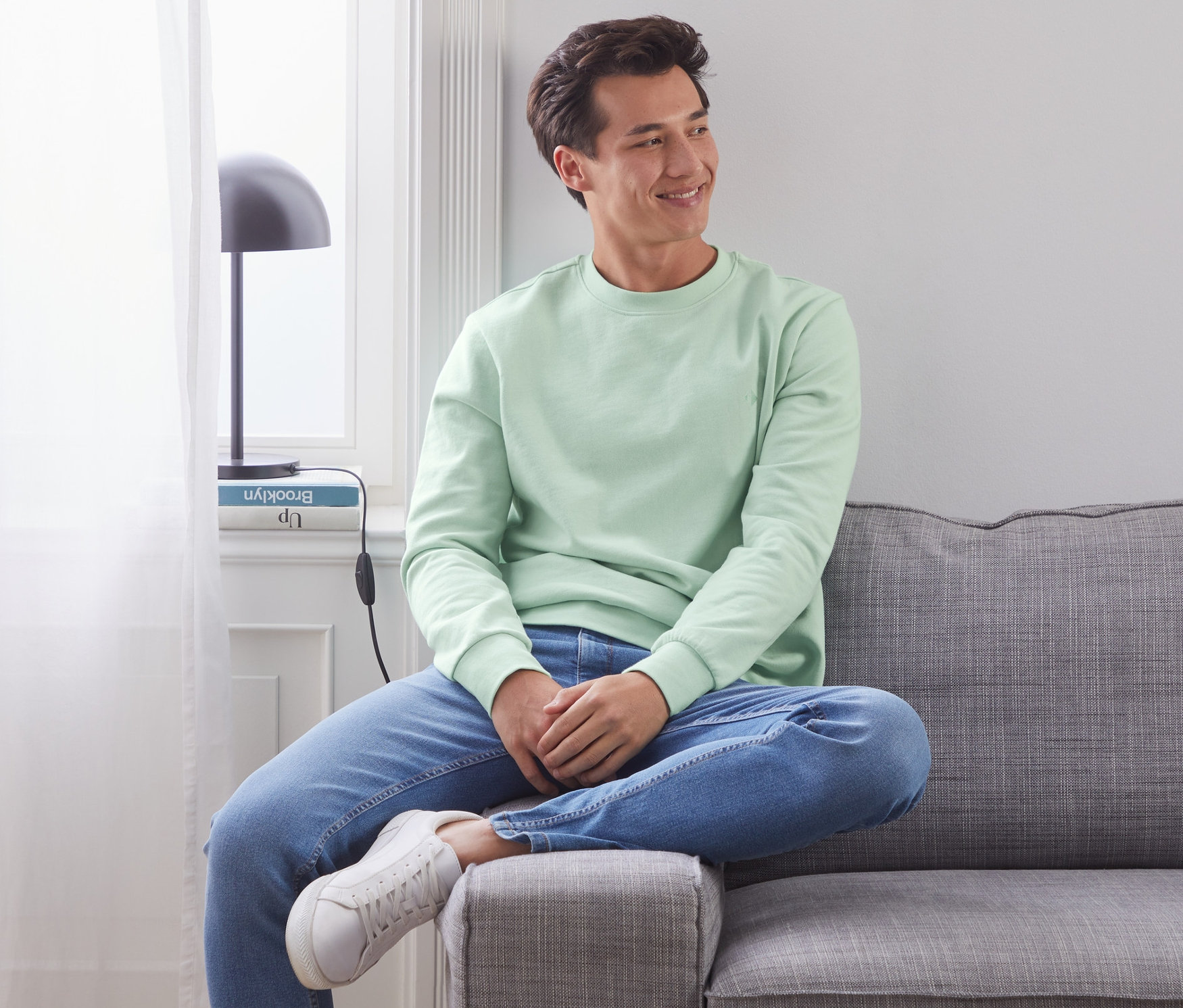 Mann sitzt auf einem grauen Sofa und trägt ein grünes Sweatshirt.