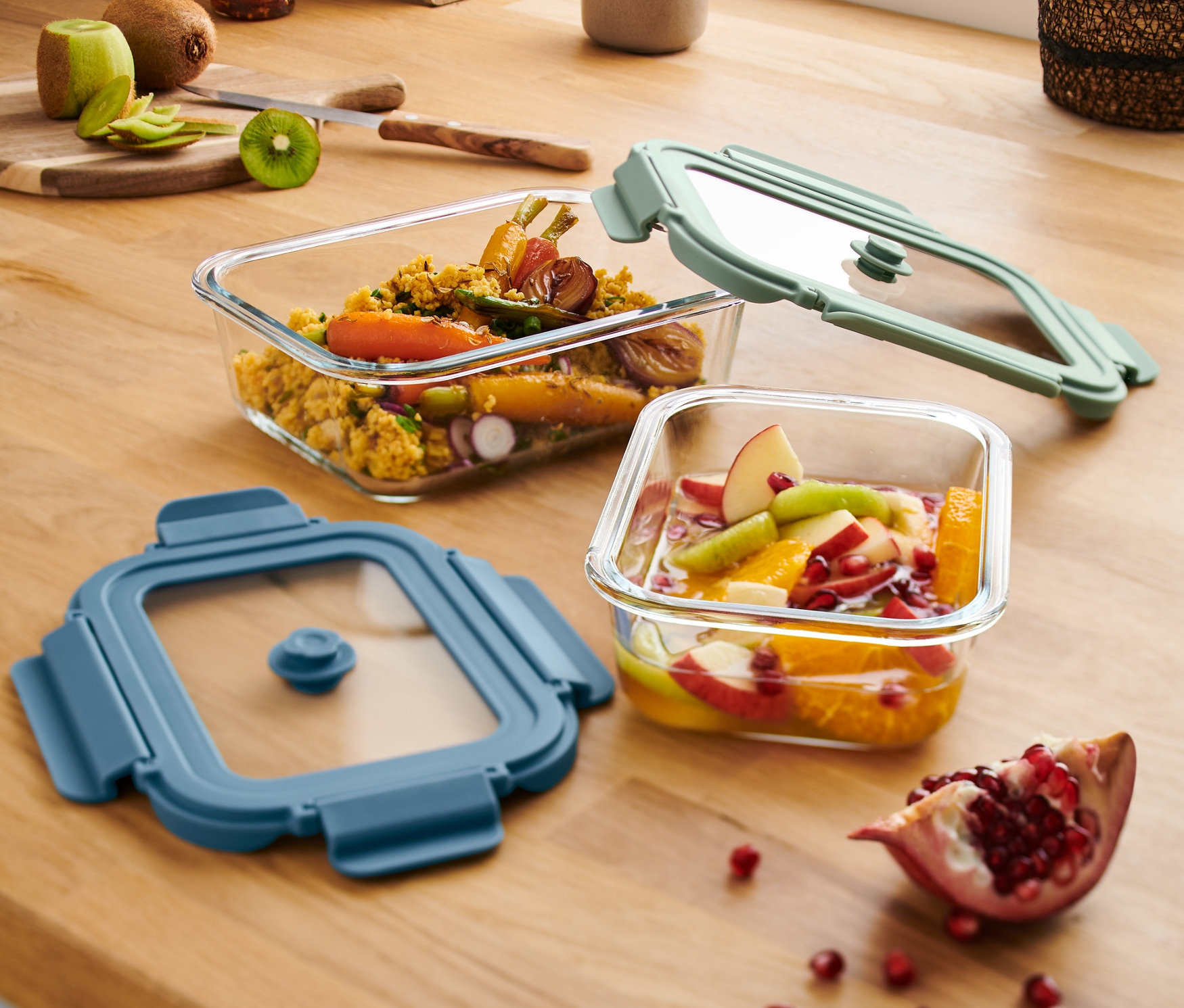 Zwei Glas-Auflaufformen mit Deckel stehen auf einer Holzoberfläche. Eine Form ist mit Gemüse, die andere mit Früchten gefüllt.