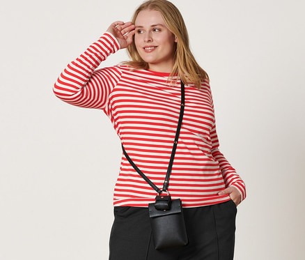 Frau posiert in einem rot-weiß gestreiften Langarmshirt, einer schwarzen Joggpants mit Biese, Ledersneakern und einer Mini-Tasche über der Schulter.