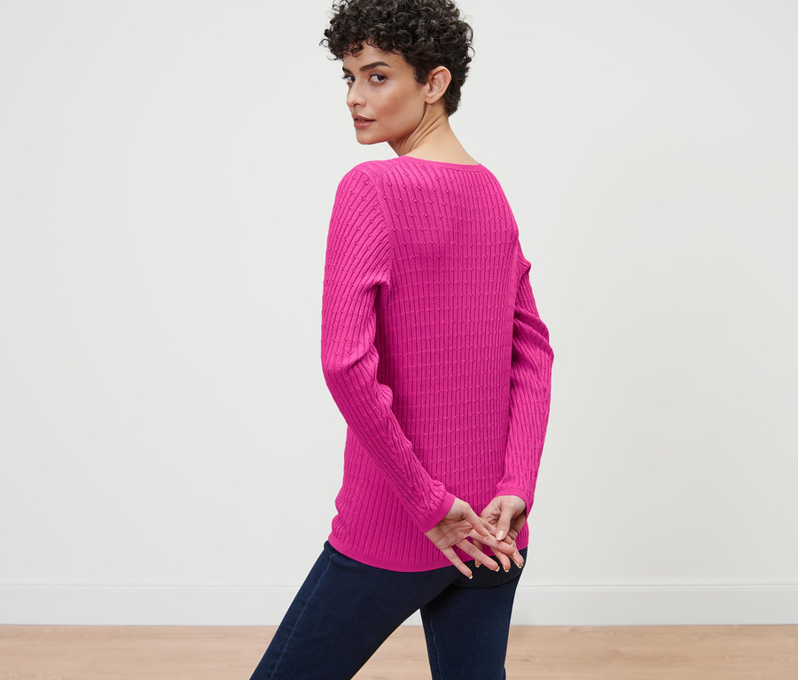 Eine Frau blickt über die Schulter und trägt einen pinken Zopfstrickpullover.