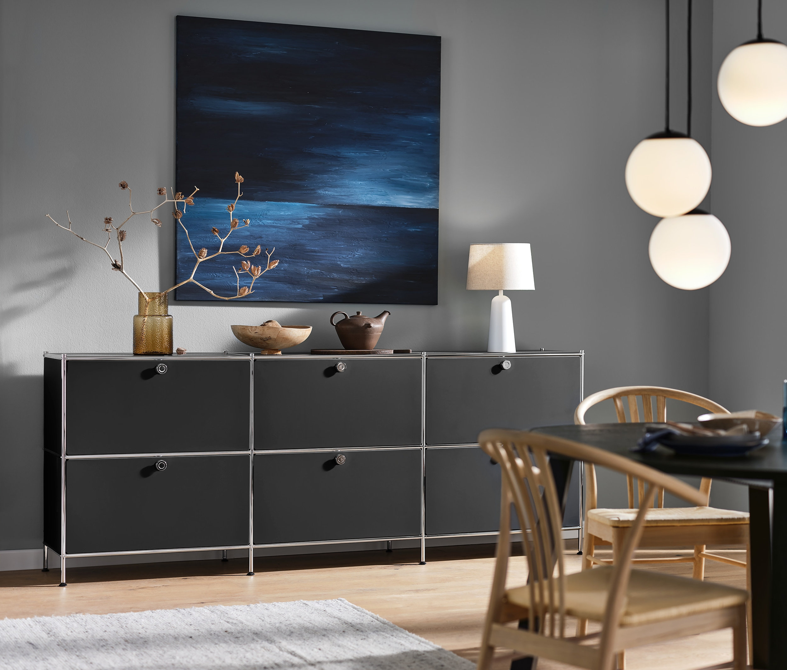 Schwarzes Sideboard »CN3« mit 6 Klappen, eine weiße Tischleuchte mit Textilschirm und eine 3-flammige Hängeleuchte mit Glaskugeln.