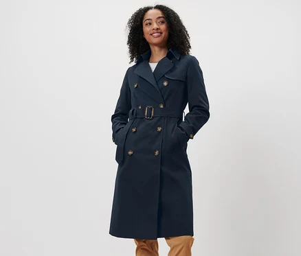 Eine Frau mit dunklen Haaren steht und trägt einen marineblauen Trenchcoat.