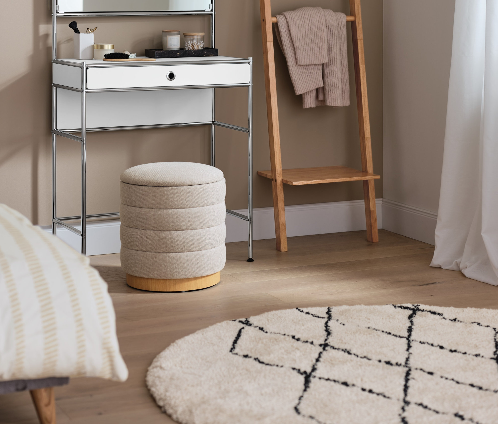 Ein Schminktisch Metall »CN3« mit Spiegelfläche steht neben einem Leiterregal. Im Vordergrund befindet sich ein 2-in-1-Pouf mit Stauraum und ein Indoorteppich »NOMAD Rhombus Line«.