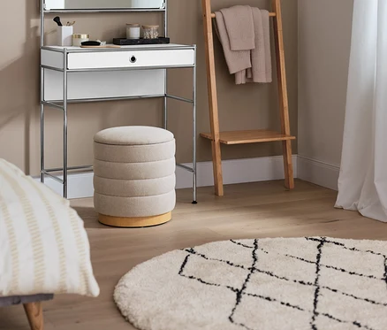 Ein Schminktisch Metall »CN3« mit Spiegelfläche steht neben einem Leiterregal. Im Vordergrund befindet sich ein 2-in-1-Pouf mit Stauraum und ein Indoorteppich »NOMAD Rhombus Line«.