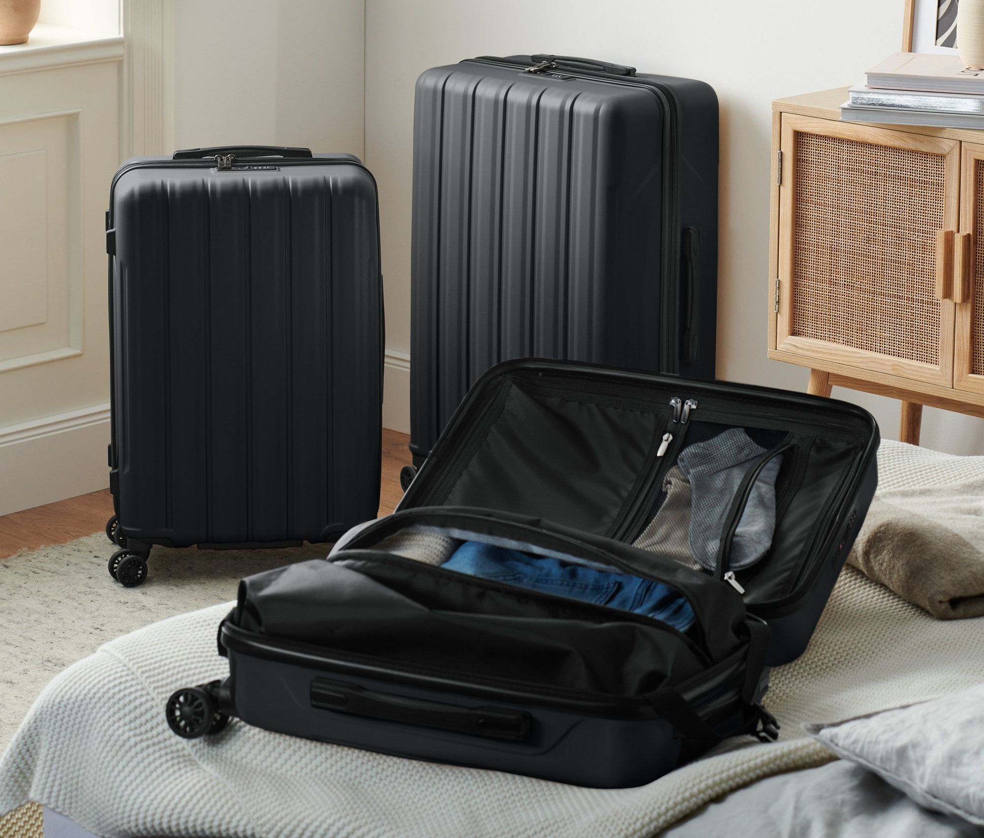 Drei schwarze Hartschalen-Koffer, einer offen auf einem Bett.