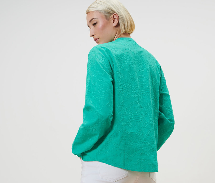Frau posiert in grüner Bluse mit Stickerei.