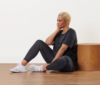 Frau sitzt in anthrazitfarbenem Sportshirt und schwarzer Wende-Sporttight auf dem Boden.