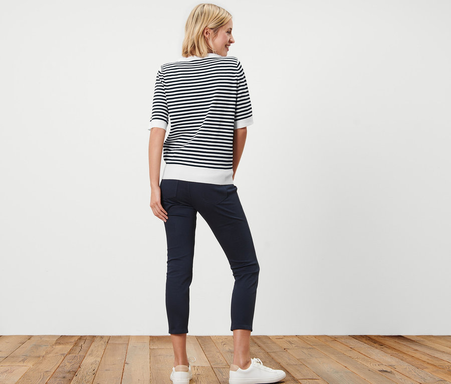 Frau von hinten in gestreiftem Feinstrickpullover, dunkelblauer Hose und weißen Turnschuhen.