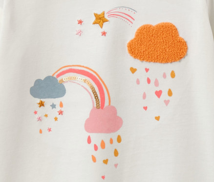 Detail eines weißen Kinder-Langarmshirts mit Regenbogen- und Wolkenmuster.