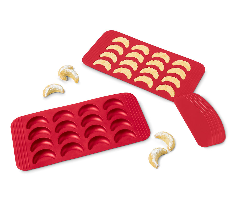 Zwei rote Vanillekipferl-Backmatten, eine mit gebackenen Kipferln gefüllt, die andere leer, und ein paar Kipferl daneben.