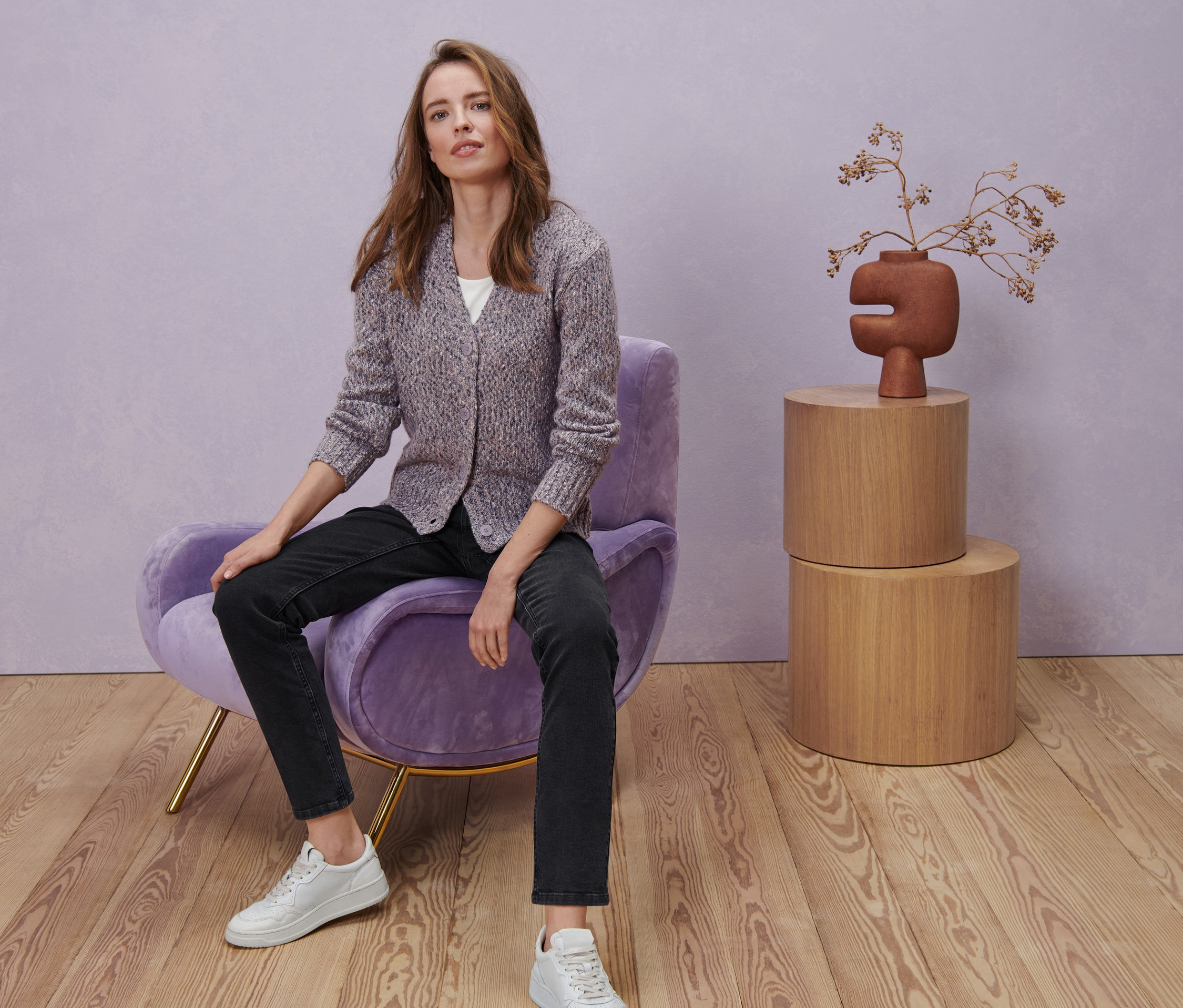 Eine Frau sitzt in einem Sessel und trägt ein weißes Halbarmshirt, eine schwarze Straight-Denim »Fit Juna« und eine Strickjacke mit Wolle.