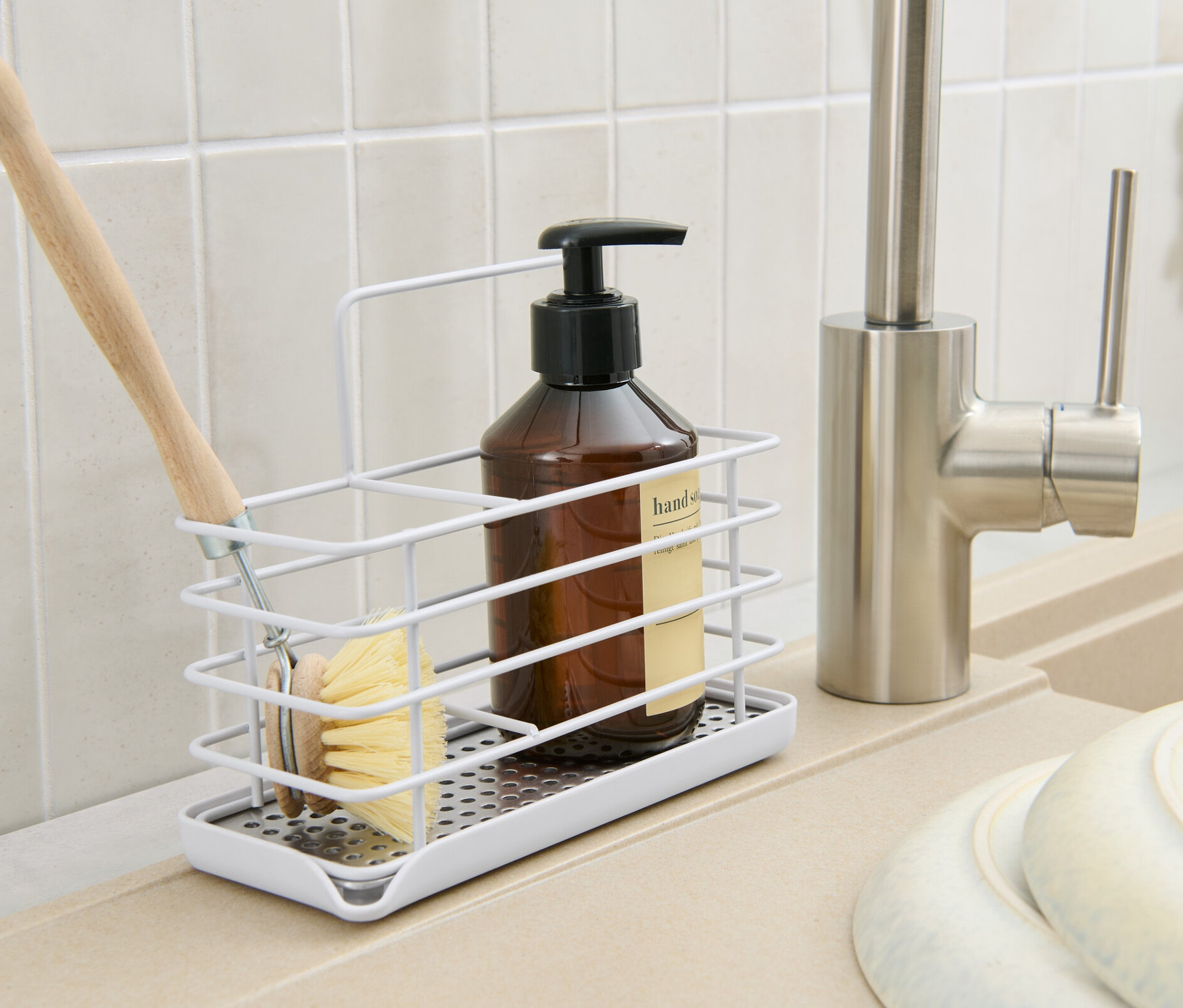 In einer Küche steht ein Spülutensilien-Ständer aus Metall mit einer Bürste, einer Flasche und einem Seifenspender.