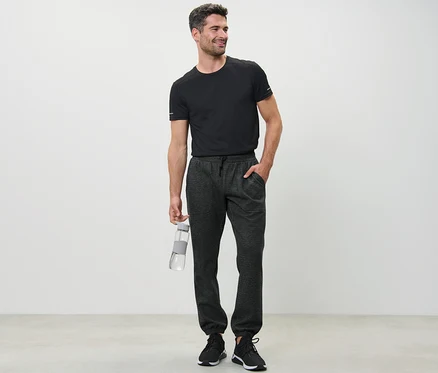 Mann im schwarzen T-Shirt hält eine Wasserflasche und trägt eine Sweathose.