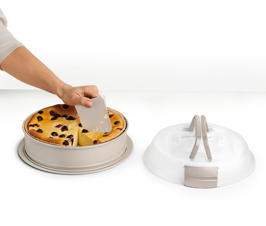 Eine Hand schneidet einen Kuchen in einer Springform mit Transportdeckel.