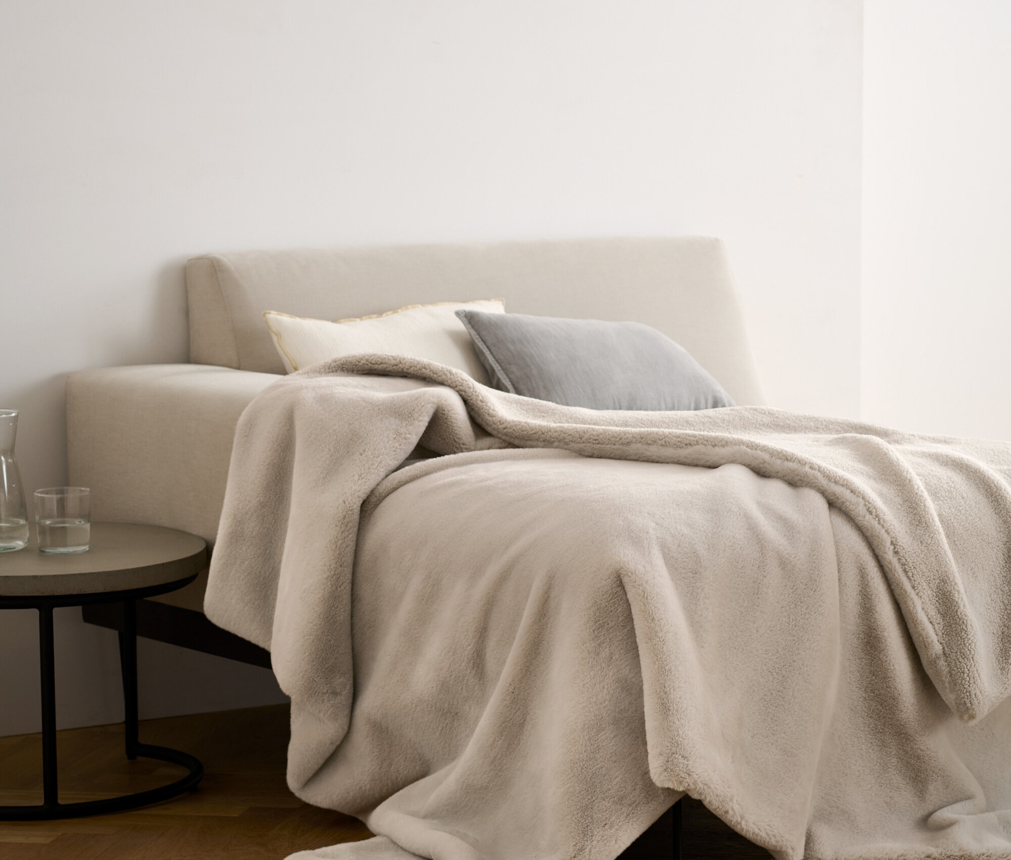 Eine beige Kuscheldecke aus Kunstfell liegt auf einem Bett mit Kissen.