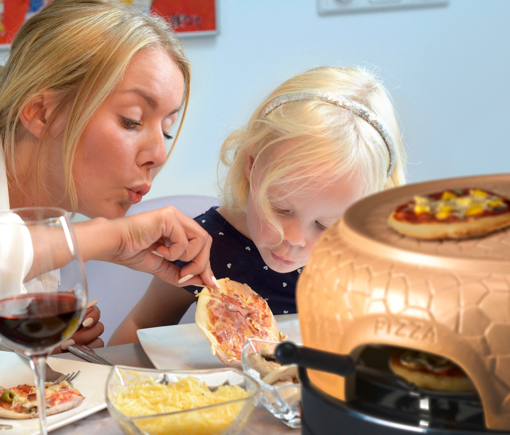 Frau und Kind essen Pizza an einem Tisch mit einem Pizzaofen, Weingläsern und einem Teller mit Pizza.