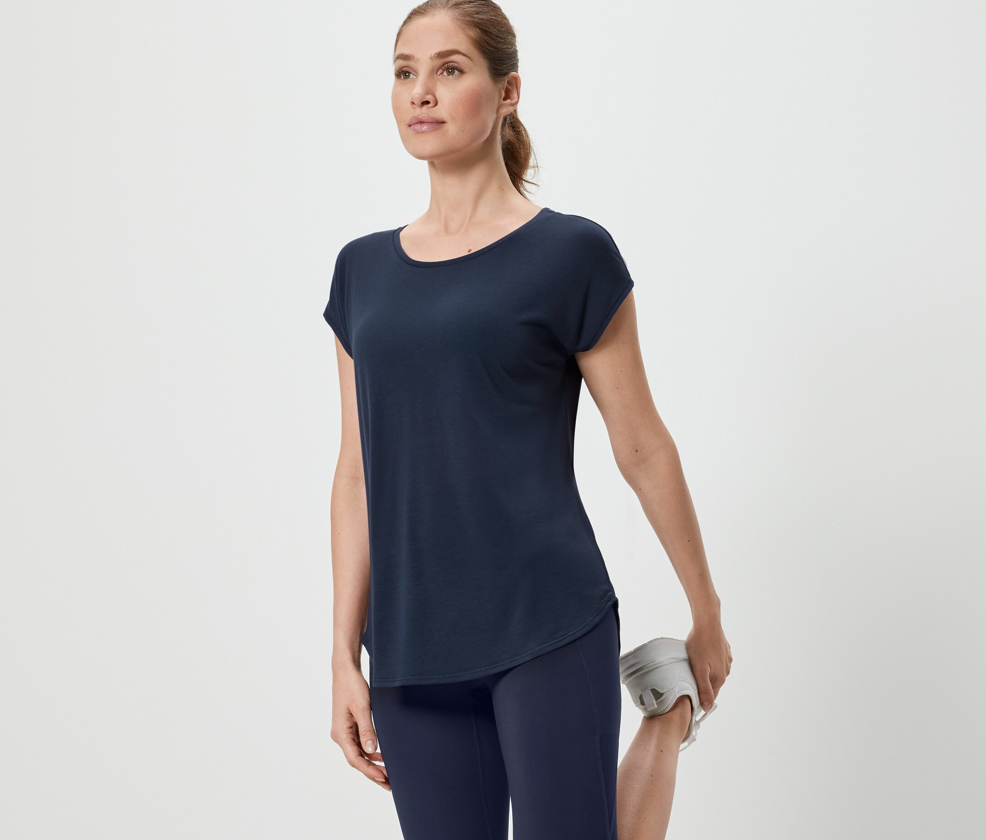 Frau dehnt Bein in blauem Sportshirt.