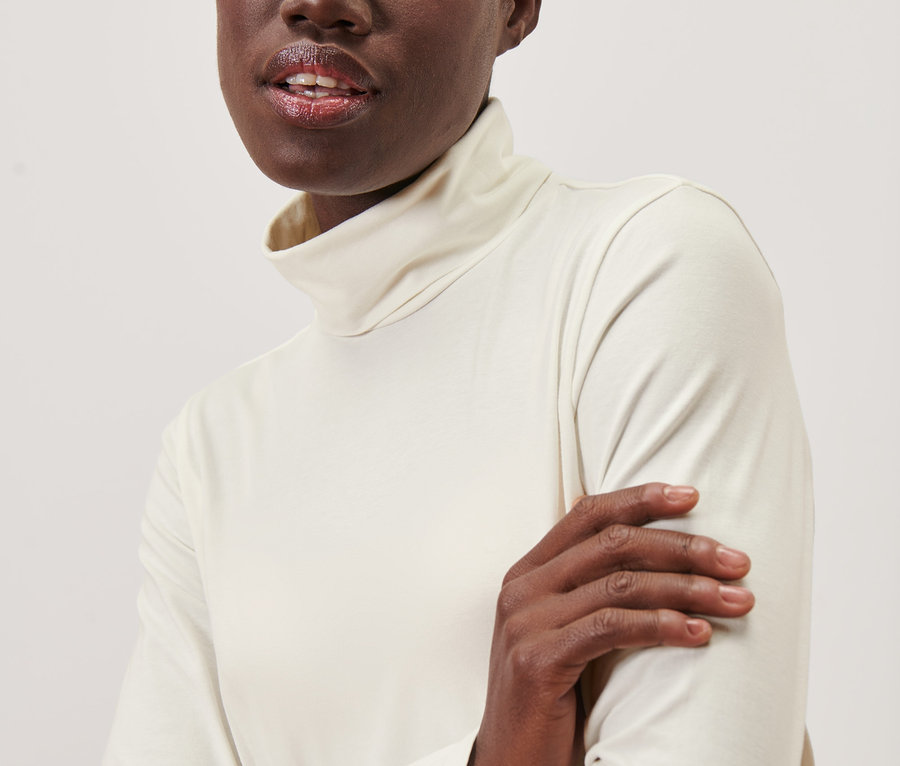 Eine Schwarze trägt ein Rollkragenshirt in Creme.