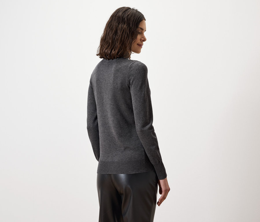 Rückansicht einer Frau mit braunem, gewelltem Haar in grauem Pullover und schwarzen Lederhosen.